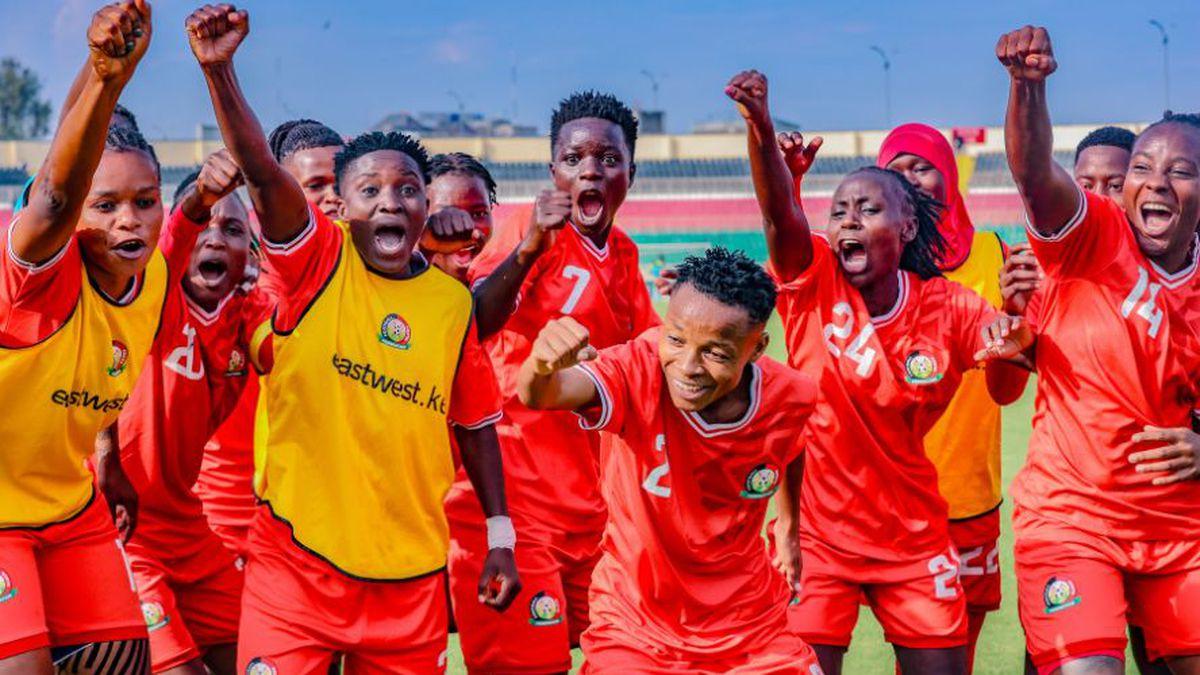 Harambee Starlets players in red Kenya jerseys celebrate together on the football pitch.
